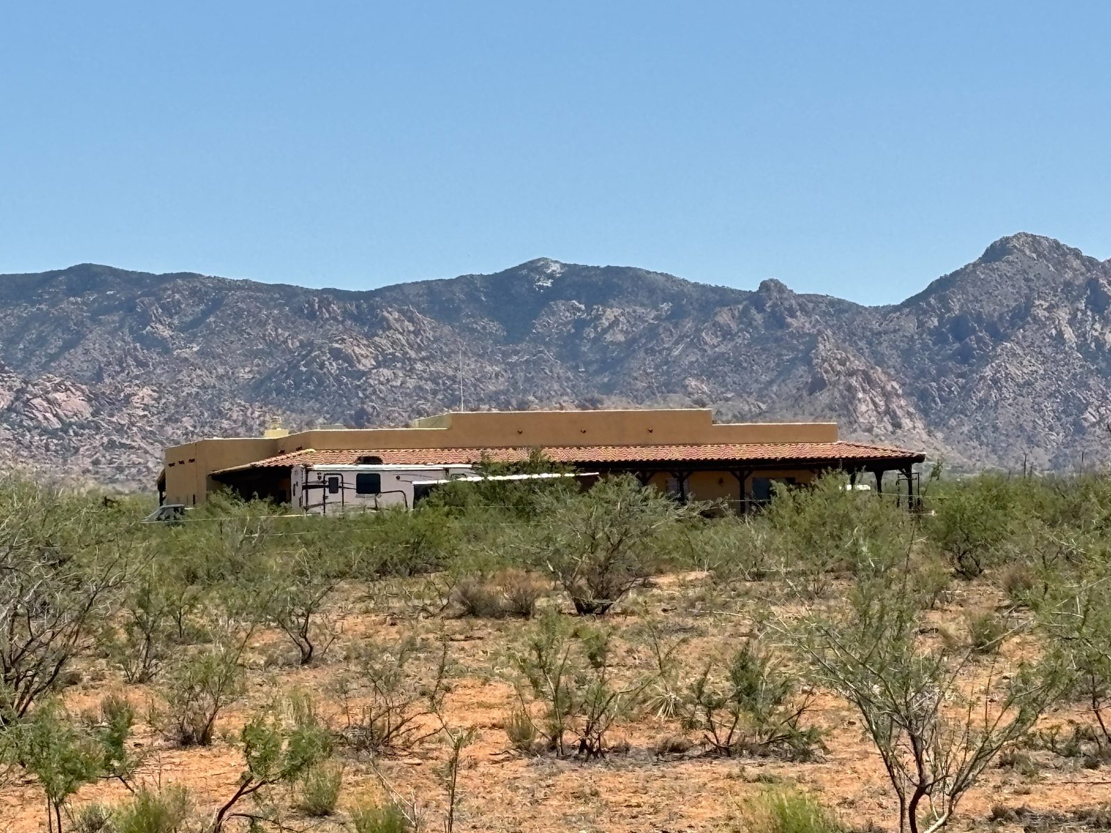 A tan stucco ranch house with a tile roof, the Dragoon Mountains rising behind it